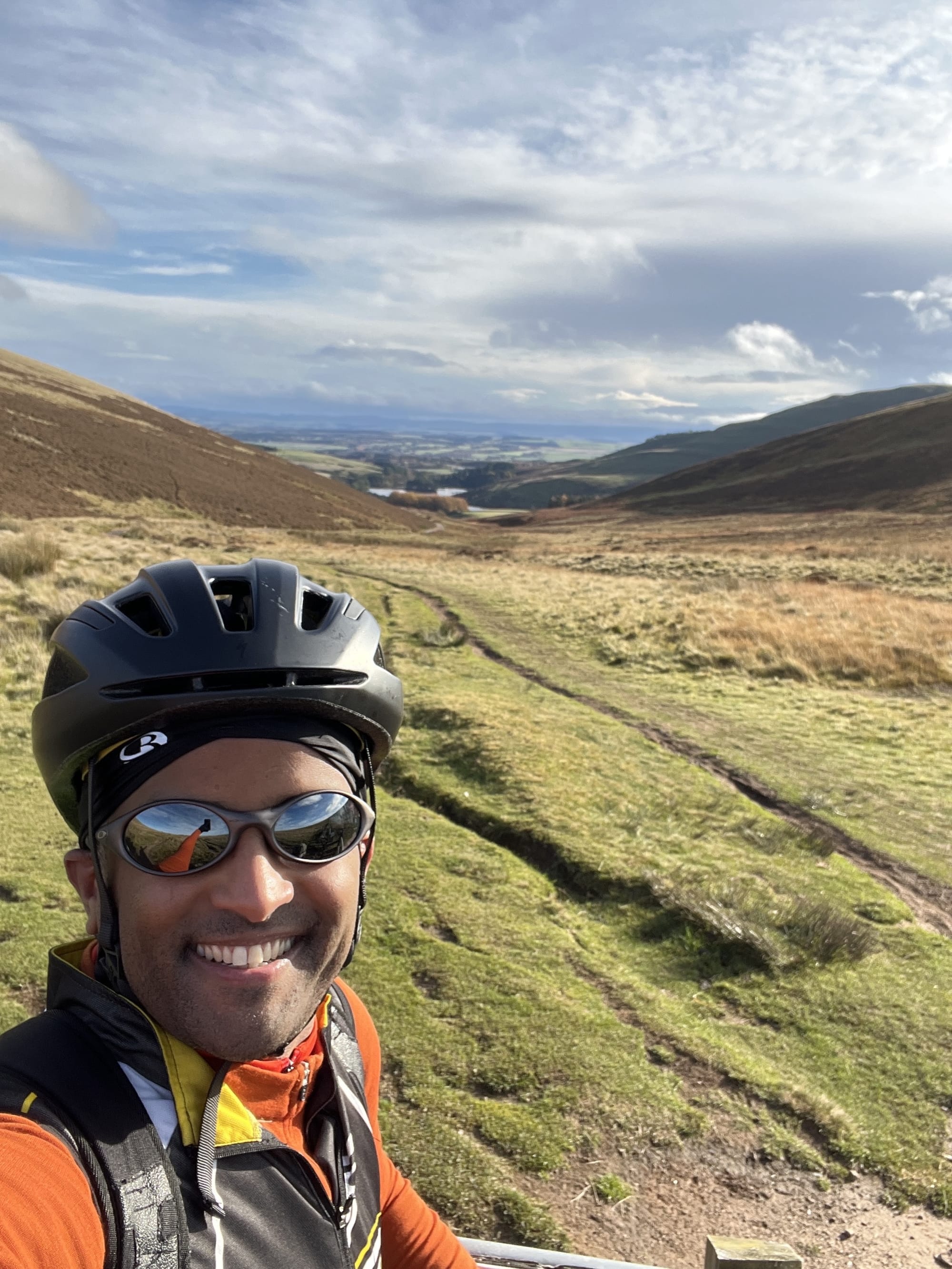 Ahmed at the the top of a moor near Pentland Hills overlooking the horizon with a reservoir at the bottom of a grassy trail