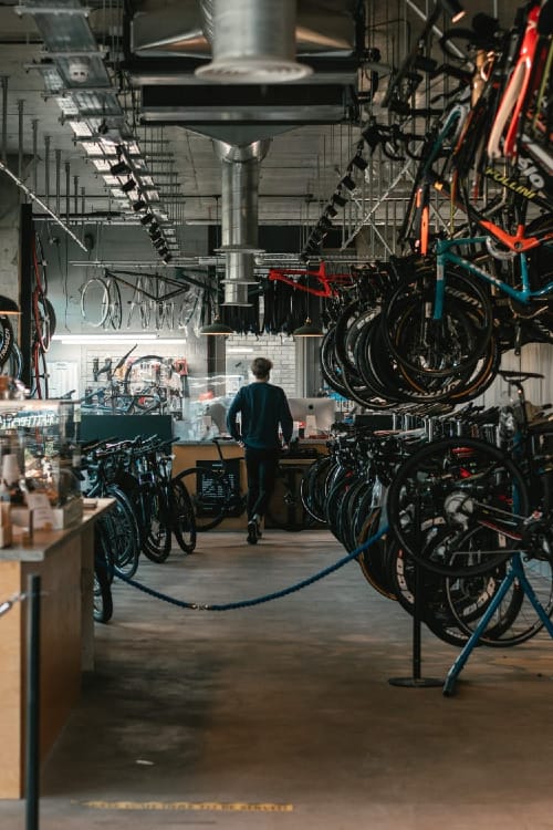 Man in black t-shirt walking between stacks and rows of bicycles in a workshop